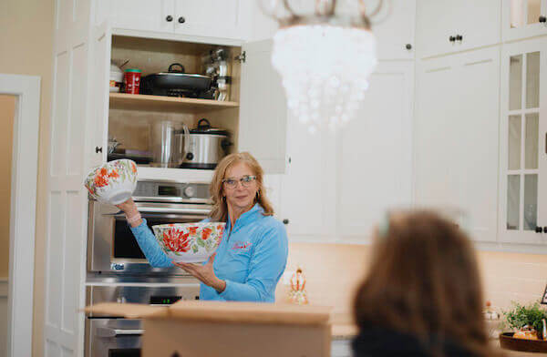 Cheryl holds dishes from a cabinet as she carries out a kitchen organization project in Bloomington