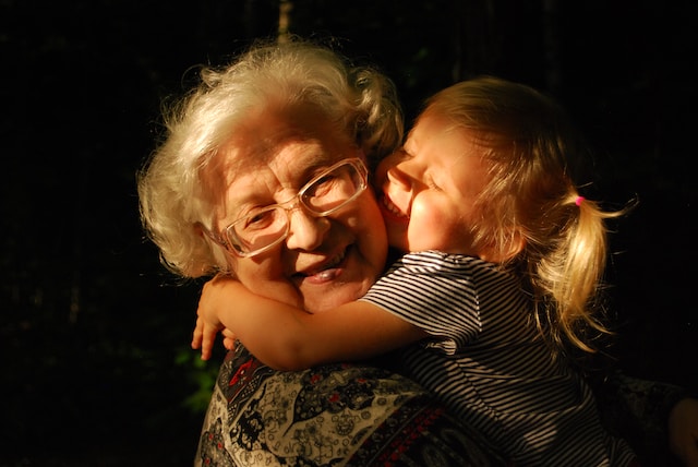 A young child hugs an elderly lady who is smiling